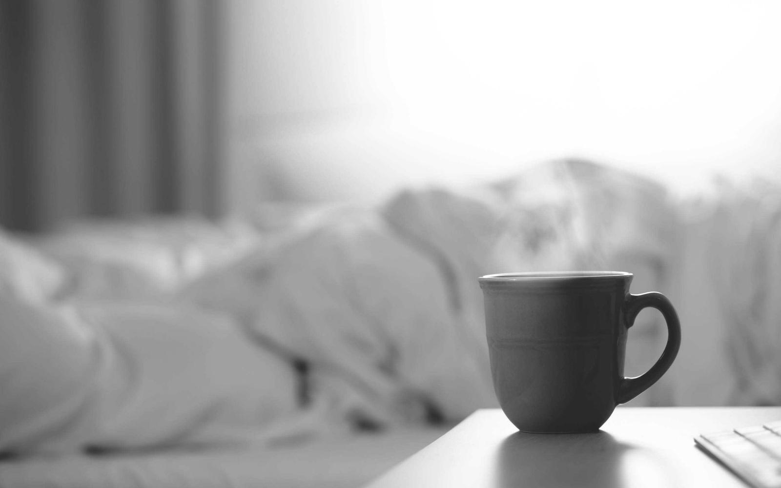Rumpled white bedding beside a bedside table, in black and white