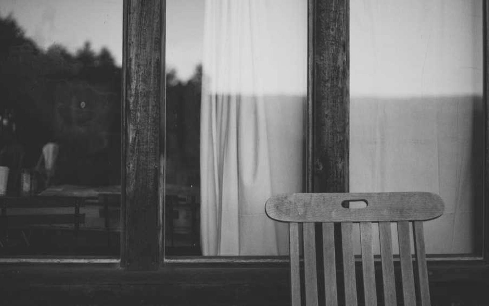 A wooden chair by a curtained window at dusk